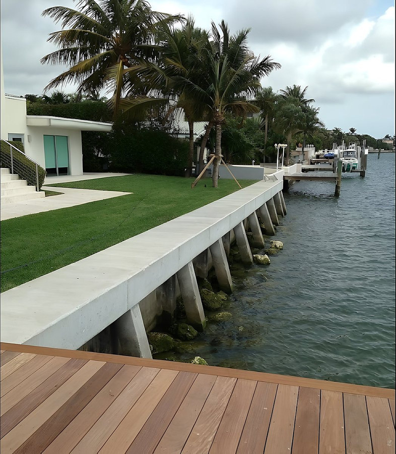 Completed concrete seawall cap with timber deck foreground and lush lawn — South Florida by Contour Marine